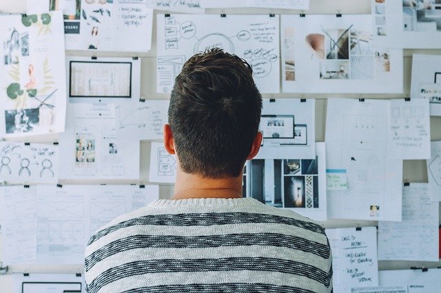 Homme réfléchissant tout en regardant une série de notes sur le mur.  Image illustrative pour la polarisation et les opinions politiques