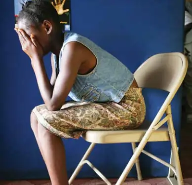 Image d'une adolescente noire assise sur une chaise couvrant son visage.